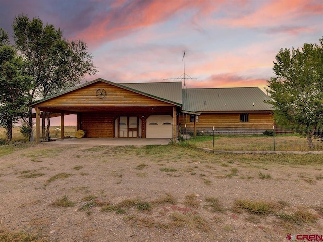 view of front facade featuring fence, dirt driveway, an attached garage, metal roof, and a carport
