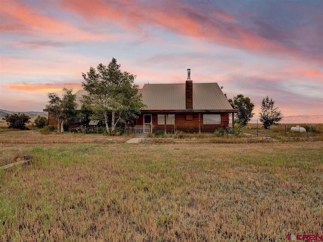 back of house at dusk featuring a chimney and metal roof