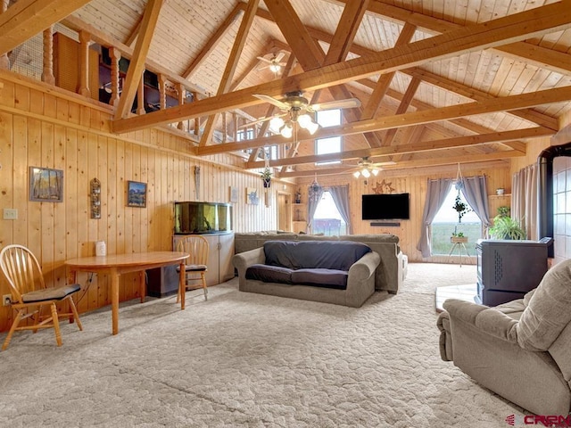 living area featuring a ceiling fan, carpet, high vaulted ceiling, wooden walls, and beamed ceiling