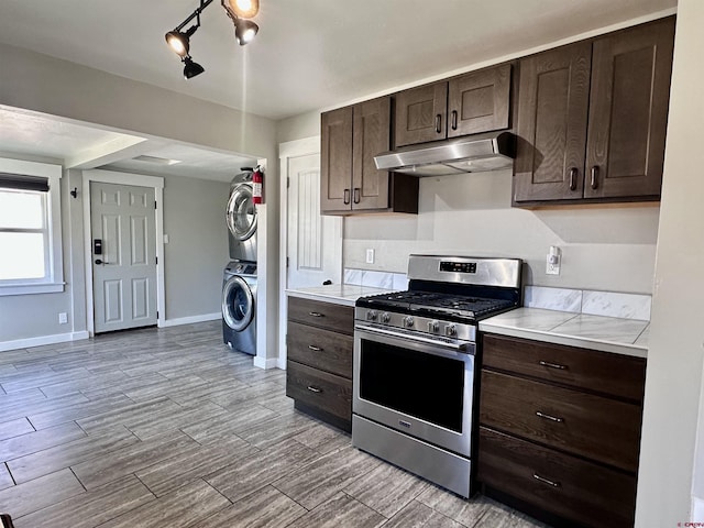 2375 W 2nd Ave, Durango, CO 81301 - kitchen featuring stainless steel gas range oven, stacked washing machine and dryer, under cabinet range hood, dark brown cabinets, and baseboards