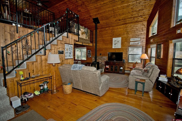 living area with high vaulted ceiling, a wood stove, wooden walls, stairs, and wood-type flooring