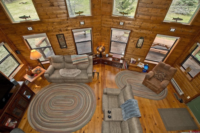 living area with a towering ceiling, wood walls, hardwood / wood-style floors, and healthy amount of natural light
