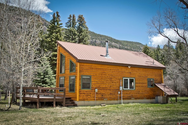 rear view of property with a wooden deck, a yard, a view of trees, central air condition unit, and metal roof