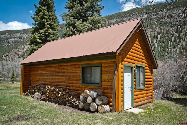 view of side of property featuring a wooded view, log veneer siding, an outbuilding, and metal roof