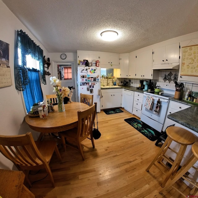 230 NW 5th St, Cedaredge, CO 81413 - kitchen with white appliances, under cabinet range hood, light wood-style floors, a textured ceiling, and dark countertops