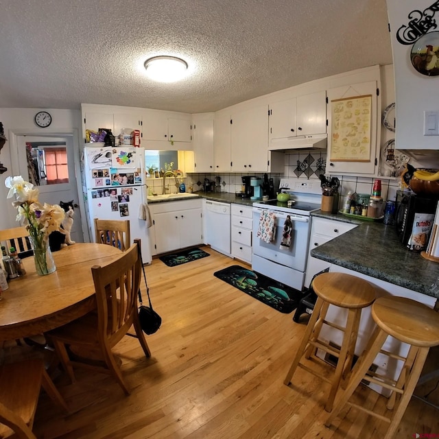 230 NW 5th St, Cedaredge, CO 81413 - kitchen with white appliances, under cabinet range hood, light wood finished floors, a textured ceiling, and dark countertops