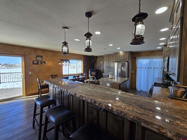 4189 Crowther Ln, Alamosa, CO 81101 - kitchen featuring a wood stove, appliances with stainless steel finishes, a kitchen bar, dark wood-style flooring, and a textured ceiling