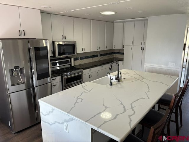 541 Perry Dr, Pagosa Springs, CO 81147 - kitchen featuring stainless steel appliances, a sink, dark wood-style flooring, white cabinets, and a kitchen bar