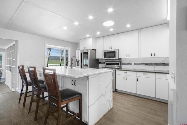 541 Perry Dr, Pagosa Springs, CO 81147 - kitchen with appliances with stainless steel finishes, a kitchen bar, a center island with sink, white cabinets, and light wood-style flooring