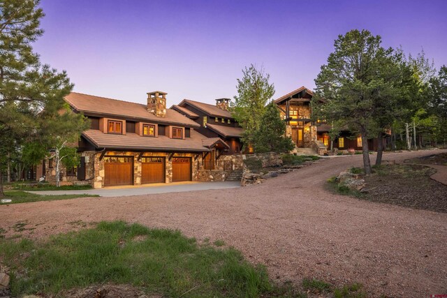 182 Juniper Rd S, Ridgway, CO 81432 - view of front facade featuring curved driveway, stone siding, an attached garage, a chimney, and a tile roof
