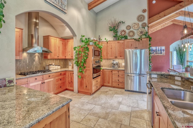 520B Whispering Wood Dr, Pagosa Springs, CO 81147 - kitchen featuring appliances with stainless steel finishes, wall chimney range hood, beamed ceiling, arched walkways, and decorative backsplash