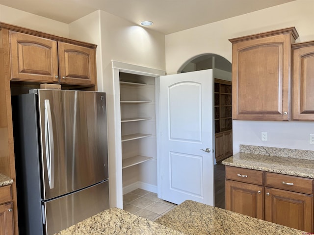 1252 Peppertree Dr, Montrose, CO 81401 - kitchen with freestanding refrigerator, light tile patterned flooring, light stone counters, and brown cabinetry