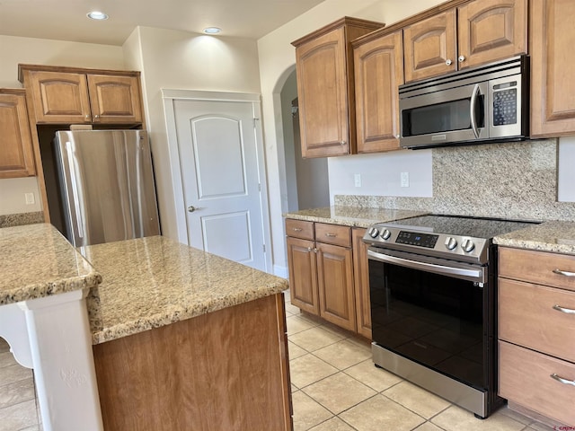 1252 Peppertree Dr, Montrose, CO 81401 - kitchen featuring appliances with stainless steel finishes, light stone counters, arched walkways, brown cabinets, and recessed lighting