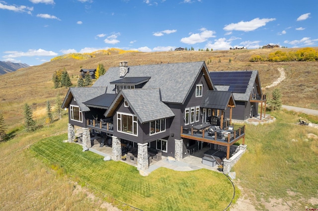 905 County Road 317, Crested Butte, CO 81224 - back of property with a patio, solar panels, a lawn, a deck with mountain view, and a standing seam roof