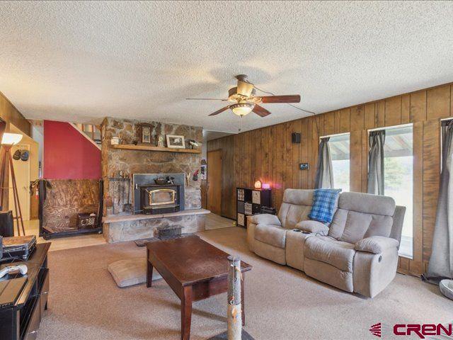 157 S Primrose Ridge Pl, Pagosa Springs, CO 81147 - carpeted living room with wooden walls, a ceiling fan, a textured ceiling, and a wood stove