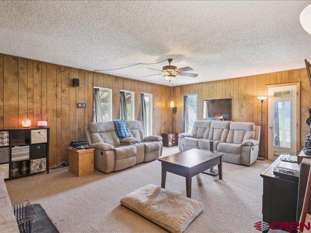 157 S Primrose Ridge Pl, Pagosa Springs, CO 81147 - living room featuring a textured ceiling, light carpet, wood walls, and a ceiling fan
