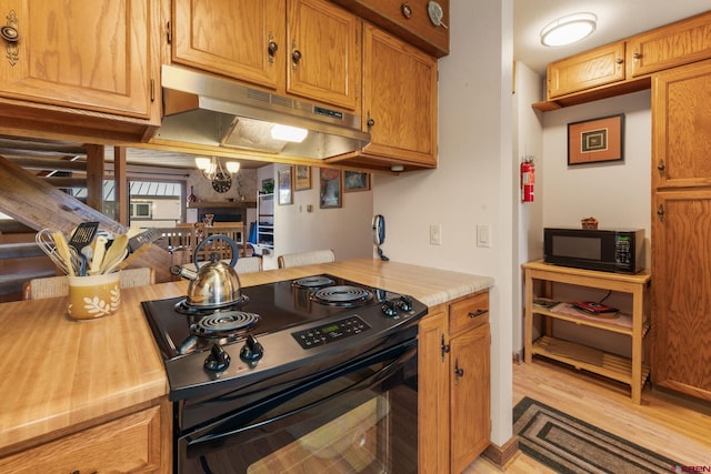 15 Marcellina Ln # 120, Mount Crested Butte, CO 81225 - kitchen with black appliances, under cabinet range hood, light wood-type flooring, and brown cabinetry