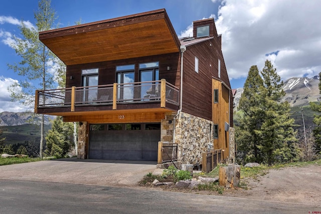 123 Boulders Way, Mountain Village, CO 81435 - view of front of house featuring stone siding, a balcony, an attached garage, concrete driveway, and a mountain view