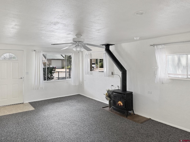 135 N 4th St, Hotchkiss, CO 81419 - unfurnished living room featuring a textured ceiling, ceiling fan, a wood stove, carpet flooring, and baseboards