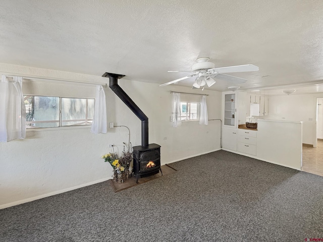 135 N 4th St, Hotchkiss, CO 81419 - unfurnished living room with a wood stove, a textured ceiling, a ceiling fan, baseboards, and dark colored carpet