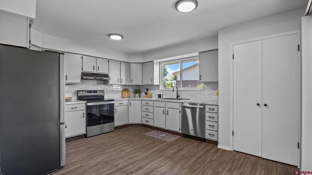 2130 Hartford Way Unit C, Montrose, CO 81401 - kitchen with appliances with stainless steel finishes, under cabinet range hood, dark wood-style flooring, tasteful backsplash, and light stone counters