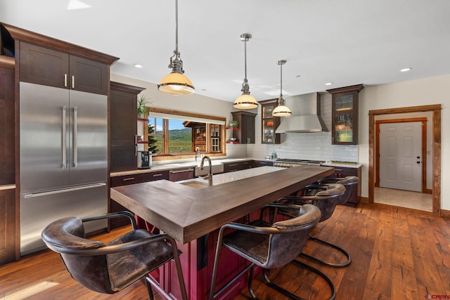 322 Wapiti Ln, Crested Butte, CO 81224 - kitchen featuring appliances with stainless steel finishes, wall chimney range hood, tasteful backsplash, dark wood-style flooring, and an island with sink