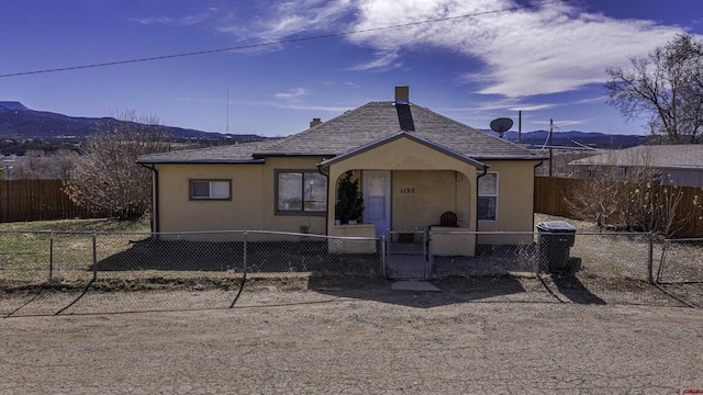 1132 Robinson Ave, Trinidad, CO 81082 - back of house with stucco siding, a fenced front yard, a chimney, a mountain view, and a gate