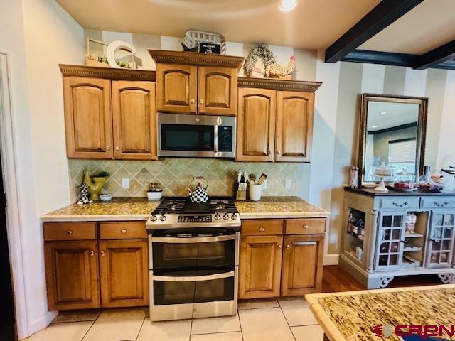 1490 SE Fairway Dr, Cedaredge, CO 81413 - kitchen with stainless steel appliances, light countertops, brown cabinets, decorative backsplash, and beam ceiling