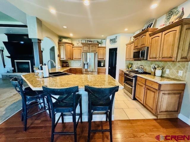 1490 SE Fairway Dr, Cedaredge, CO 81413 - kitchen featuring stainless steel appliances, a breakfast bar area, arched walkways, tasteful backsplash, and brown cabinets