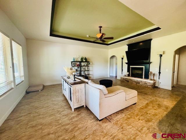 1490 SE Fairway Dr, Cedaredge, CO 81413 - living area with arched walkways, a raised ceiling, ceiling fan, and a fireplace with raised hearth