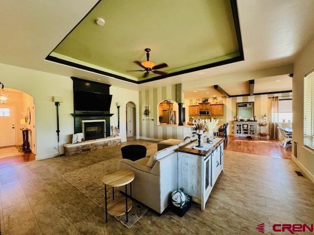 1490 SE Fairway Dr, Cedaredge, CO 81413 - living area with a raised ceiling, arched walkways, a glass covered fireplace, and a ceiling fan