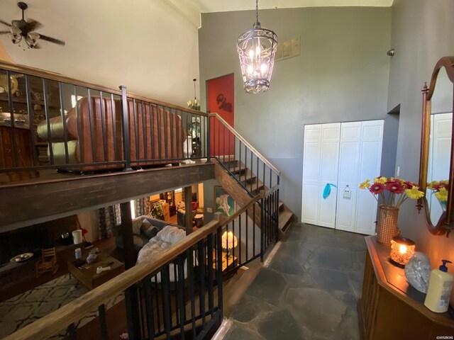 stairway featuring high vaulted ceiling, stone finish floor, and ceiling fan with notable chandelier