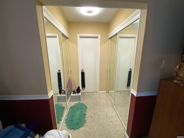 hall featuring a textured ceiling, baseboards, and light colored carpet