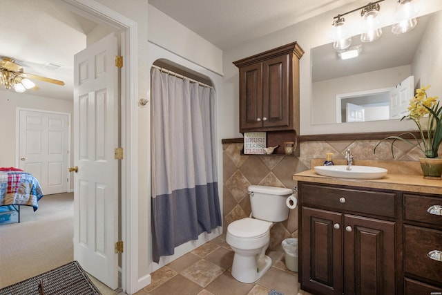 bathroom with curtained shower, toilet, vanity, tile walls, and a ceiling fan