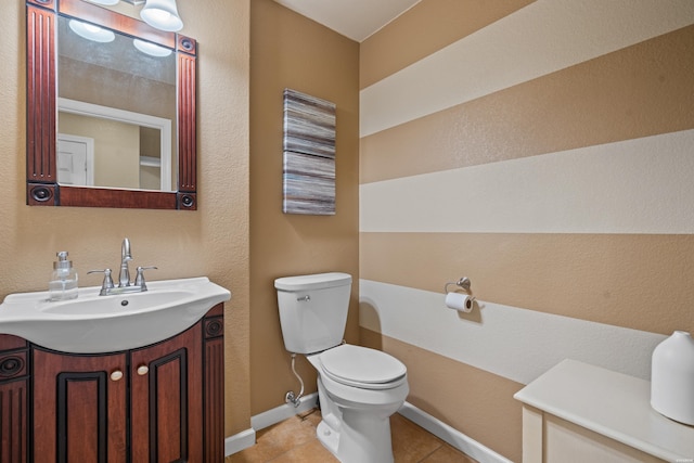 half bathroom with baseboards, vanity, toilet, and tile patterned floors