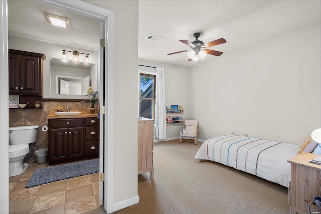 bedroom with baseboards, visible vents, light colored carpet, ensuite bathroom, and a sink