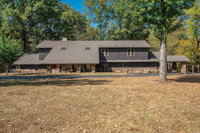 back of property with a shingled roof, stone siding, and a yard