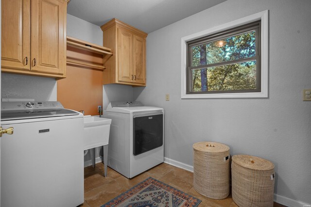 clothes washing area featuring washing machine and dryer, cabinet space, and baseboards