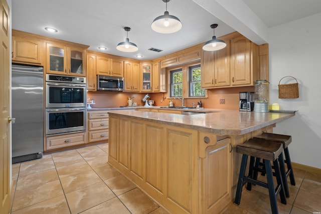 kitchen featuring a peninsula, a kitchen bar, glass insert cabinets, and stainless steel appliances