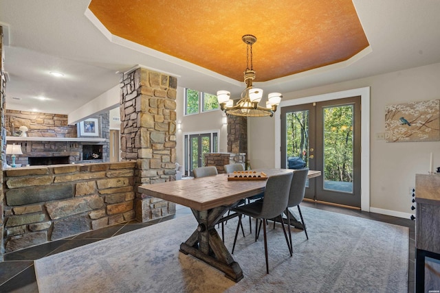 dining area with baseboards, a tray ceiling, ornate columns, a fireplace, and a notable chandelier