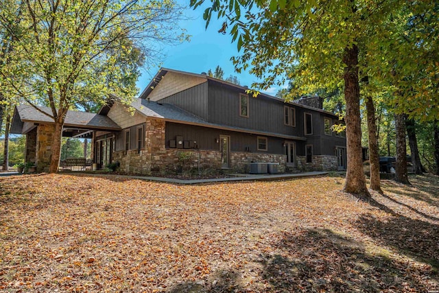 rear view of house with stone siding, a chimney, and central air condition unit