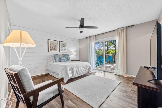 bedroom featuring a textured ceiling, ceiling fan, wooden walls, access to exterior, and light wood finished floors