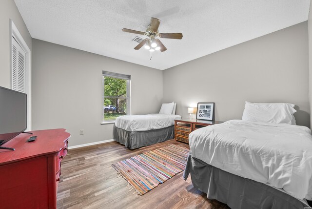 bedroom featuring a ceiling fan, a textured ceiling, baseboards, and wood finished floors