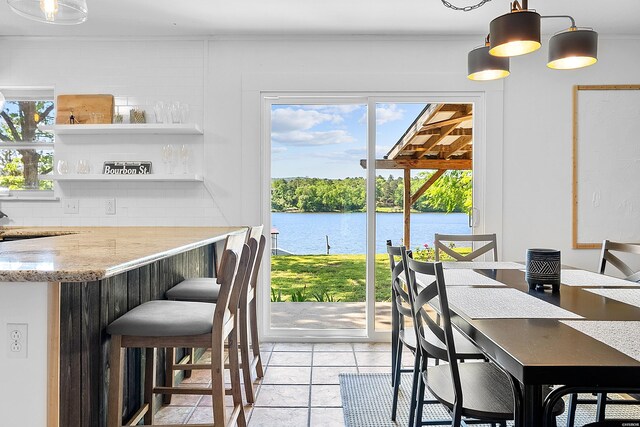 dining area with a water view, a bar, and light tile patterned floors