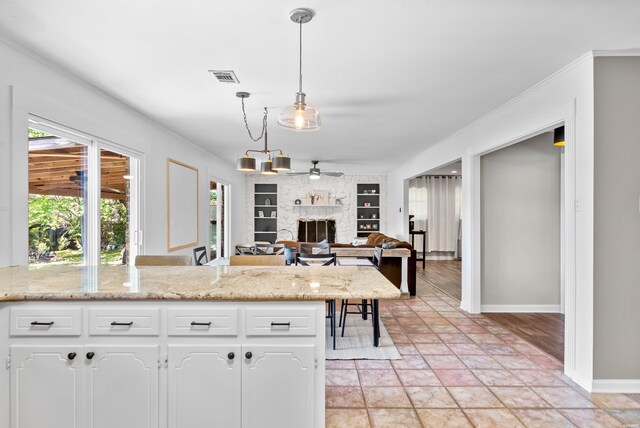 kitchen featuring visible vents, decorative light fixtures, built in shelves, white cabinetry, and a fireplace