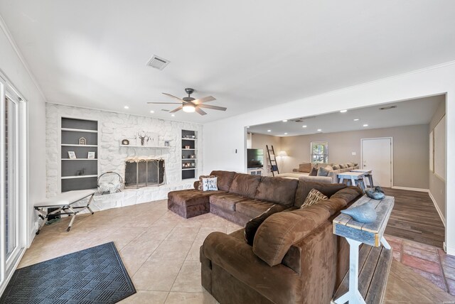 living room featuring a stone fireplace, recessed lighting, visible vents, and built in features