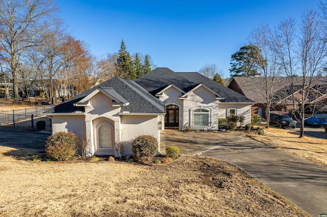 view of front of home featuring roof with shingles, fence, driveway, and stucco siding