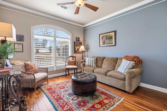 living room with visible vents, wood finished floors, crown molding, baseboards, and ceiling fan