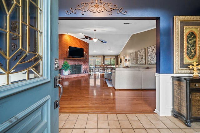 foyer with light tile patterned floors, visible vents, ceiling fan, vaulted ceiling, and a fireplace