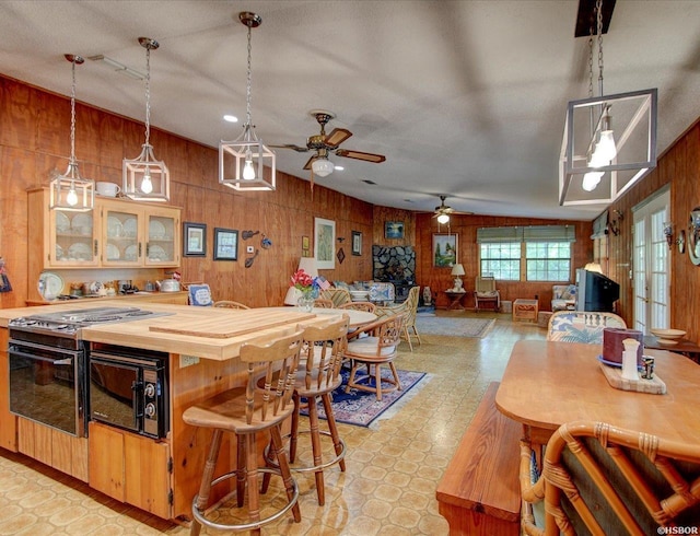 interior space featuring a ceiling fan, butcher block countertops, black microwave, light floors, and wood walls